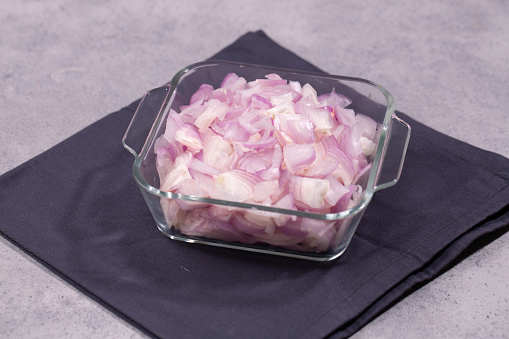 Chopped Onion arranged in a square glass bowl placed on grey color napkin with cement grey background, isolated , top view.