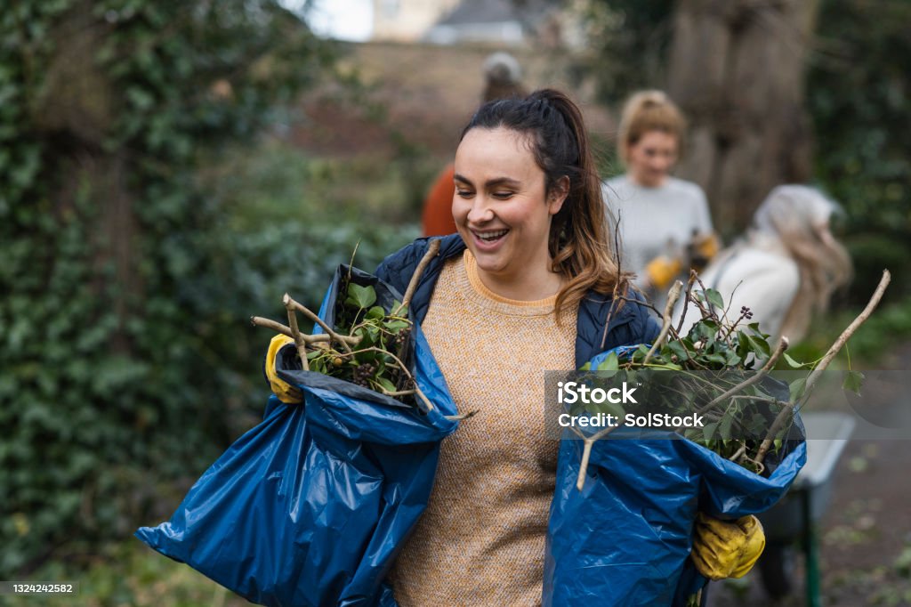 Zero Waste Gardening A front view of a young brunette woman carrying two bags of garden waste that is to be composted and reused. She is working on a community space garden in Hexham in the North East of England with a group of friends. Volunteer Stock Photo
