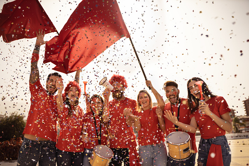 Football fan screaming, with red shirts out of the stadium throwing confetti. Group of young people very excited about football. Sport and fun concept. Image