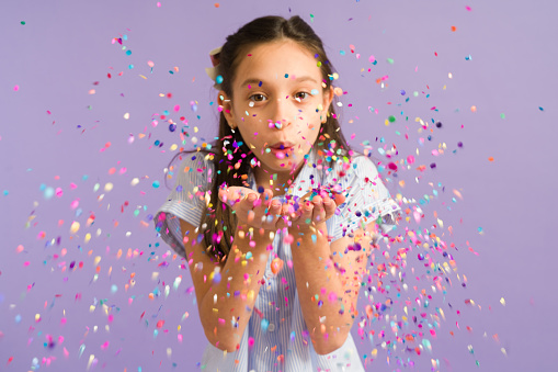 Adorable young girl blowing and playing with confetti during a happy celebration. Beautiful girl celebrating her birthday
