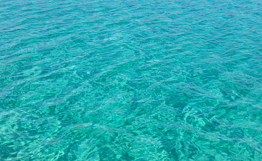 Turquoise blue color crystal clear sea water background, some reflections. Calm surface with small ripples, Summer vacation at tropical paradise.