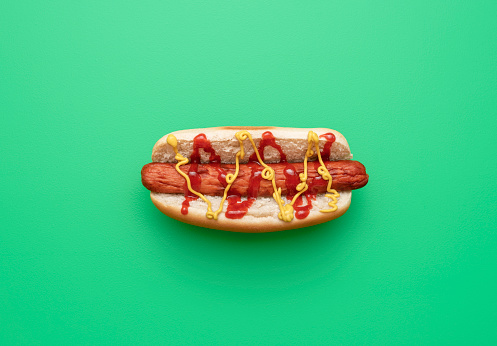 Homemade hot dog above view on a green table. One hot dog with ketchup and mustard isolated on a colored background.