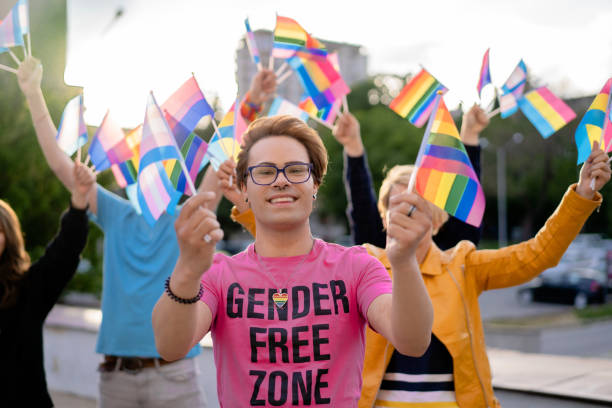 Portrait of an LGBTQ+ activist holding rainbow flags in his hands LGBTQ+ activist holding different flags of LGBTQI community defending the human rights, looking at camera non binary gender stock pictures, royalty-free photos & images
