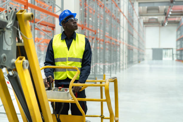 istock Young warehouse afro worker looking up operating lift machine 1324266926