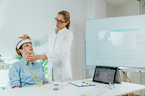 Biofeedback EEG or electroencephalograph training at a health center. Therapist monitoring brain waves using scalp sensors placed onto a client’s head