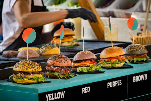 Burgers displayed in a row on street food vendor stall Various burgers displayed in a row on a wooden counter of street food vendor stall. In the background is female worker preparing ordered food. The photo was taken on a street food festivale. food festival stock pictures, royalty-free photos & images