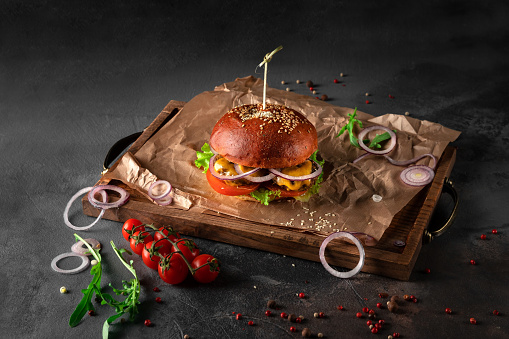 big american vegetarian burger on a black background. vegan cutlet with cheese, tomato and onion on a wooden tray, copy space