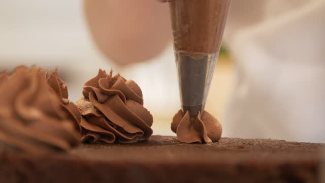 Artistic Close-Up Shot of a Young Woman's Hands Using an Icing Bag Filled with Delicious Chocolate Buttercream Frosting to Pipe Frost and Decorate a Cake