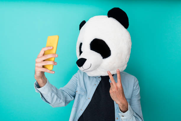 istock Happy man in panda mask taking a selfie with smartphone while gesturing victory sign over blue background 1324275869