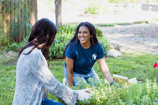 Two mid adult female friends talk and smile as they work together at the community garden.