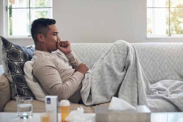 istock Shot of a young man coughing while feeling sick at home 1324276201