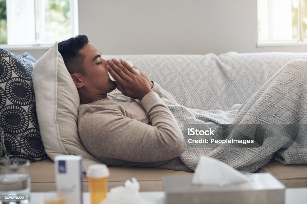 Shot of a young man blowing his nose while feeling sick at home Flu season is here Cold And Flu Stock Photo