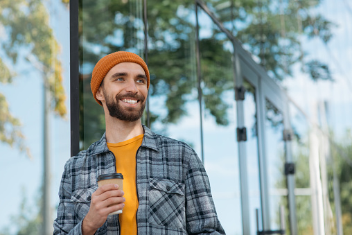 Hombre sonriente sosteniendo la taza de café para llevar mirando hacia otro lado de pie al aire libre. Concepto de coffee break photo