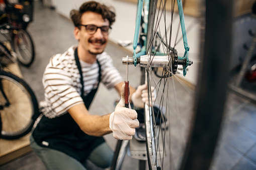 A young handsome man repairs a bicycle in his bicycle shop