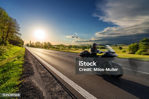 istock Motion blurred black motorcycle riding on an empty asphalt road in a rural landscape at sunset 1324281558
