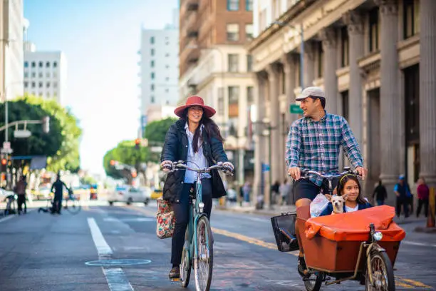 Full length view of mature mother, father, young daughter, and dog smiling at camera as they enjoy riding in open streets of downtown district.