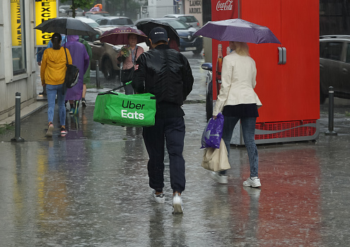 Bucharest, Romania - June 18, 2021: An Uber Eats food delivery courier, rained and soaked in water, delivers food, in rainy weather, in downtown Bucharest, Romania.