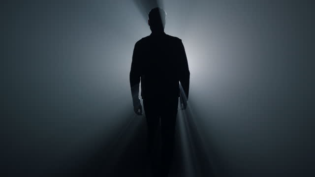 Silhouette man going away in dark background. Back view guy walking in darkness.