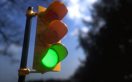Outdoor vertical traffic light with blue sky and trees around. Traffic control concept image with shallow depth of field.