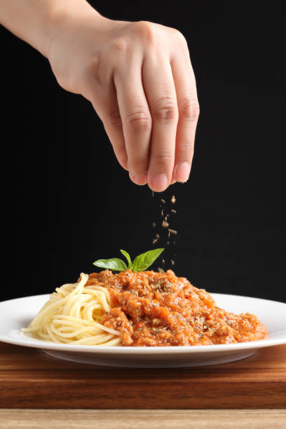 Chef sprinkle oregano in spaghetti red sauce on white dish stock photo