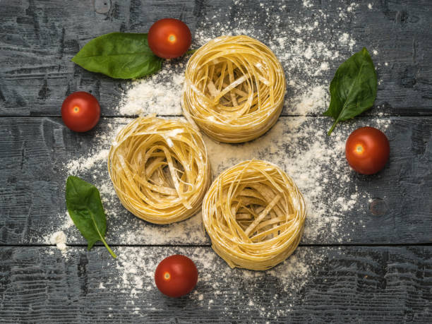 istock Rolled pasta, tomatoes and spinach leaves on a wooden table. 1324315528