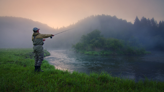 Pescador con mosca pescando en el río al amanecer brumoso photo