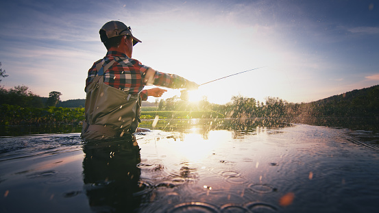 Pescador con mosca se para en el agua y lanza la mosca con caña de pescar usando Roll Cast con muchas salpicaduras photo