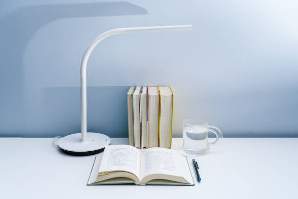 istock An open book is placed on a white table with a lamp. A stack of neatly arranged books and a transparent glass on a white table 1324326134