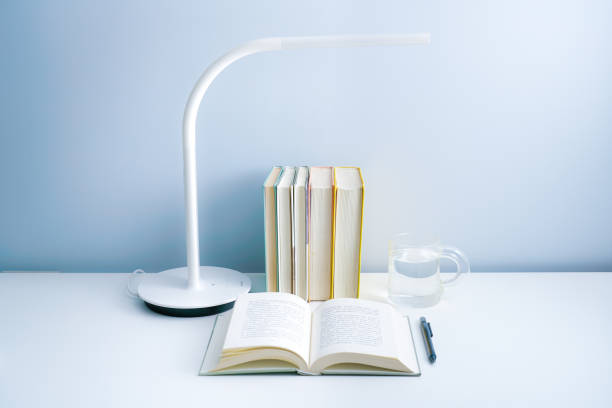 istock An open book is placed on a white table with a lamp. A stack of neatly arranged books and a transparent glass on a white table 1324326230