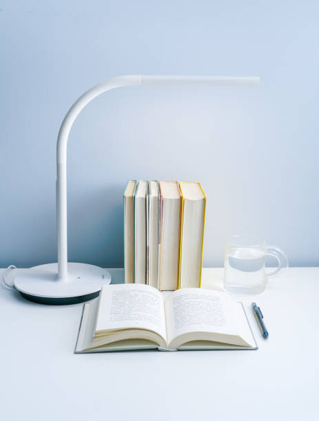 istock An open book is placed on a white table with a lamp. A stack of neatly arranged books and a transparent glass on a white table 1324326864