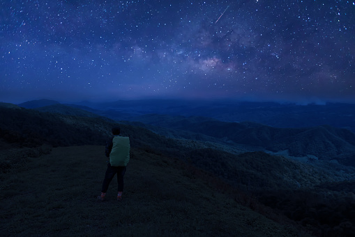 Colorful night sky with stars and silhouette of a standing man on the stone. Blue milky way with man on the mountain. High Rocks. Background with galaxy and silhouette of a man.