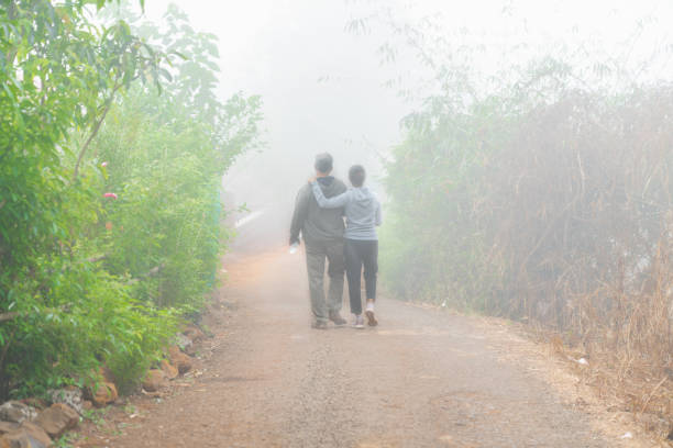 Tapola, Maharastra / India -28th December 2020 - On a misty early morning, a couple out for a walk arm around the shoulder