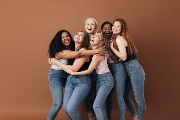 Six laughing women of a different race, age, and figure type. Group of multiracial females having fun against a brown background. stock photo