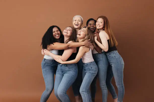 Photo of Six laughing women of a different race, age, and figure type. Group of multiracial females having fun against a brown background.