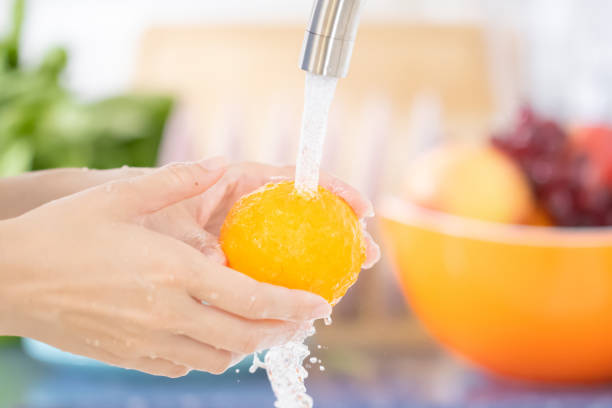 young woman washing an orange under faucet in the sink kitchen