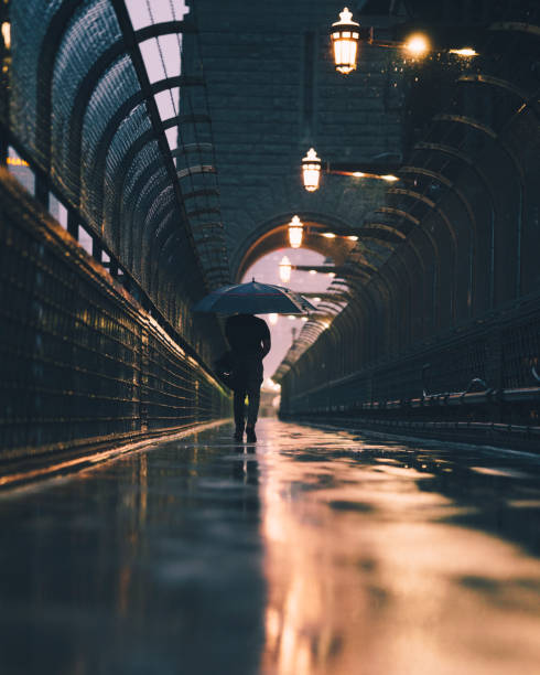 istock Man walks alone with Umbrella across bridge 1324337276