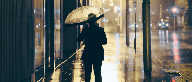 istock Man walking alone in the rain with Umbrella. City streets - empty 1324337936
