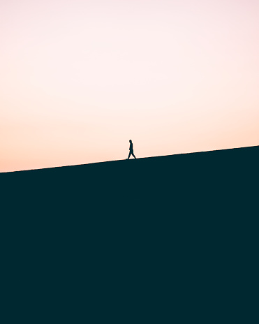 Person alone walking down hill. Silhouette.