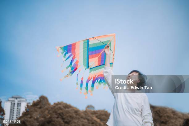 Asian Chinese Senior Woman Playing Kite In Public Park During Sunny Day Morning Stock Photo - Download Image Now