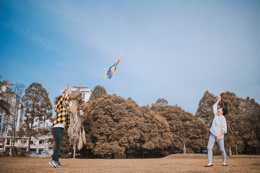 asian chinese teenage boy and his grandmother playing kite in public park during sunny day morning