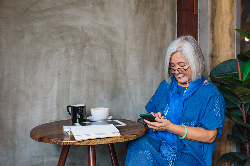 Asian senior women using smart phone while sitting at coffee shop cafe, Senior woman typing an sms message and working mobile devices, People lifestyle technology concept