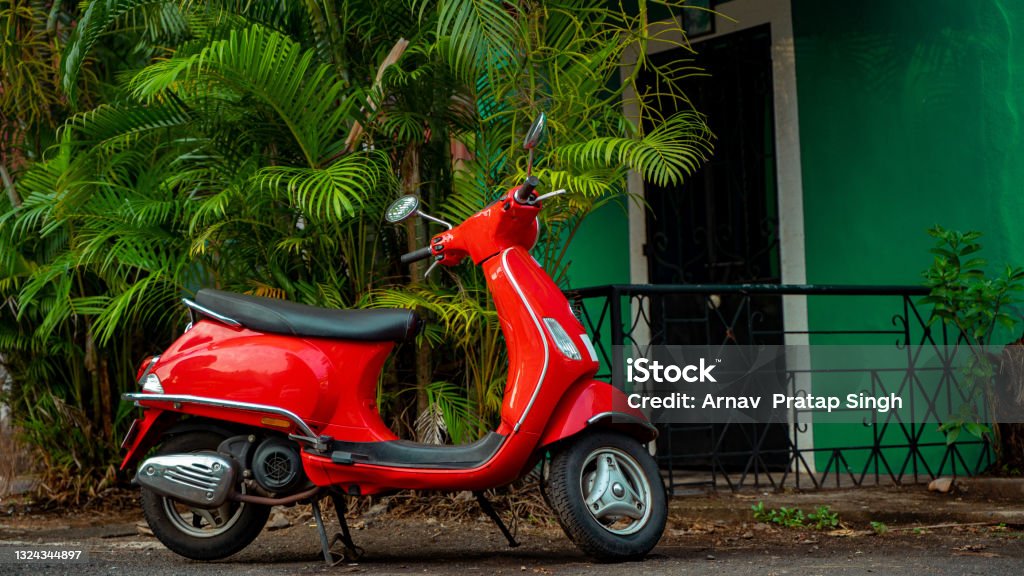 Red scooter parked against green background at the street Goa Stock Photo