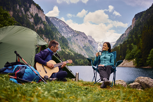 Young couple camping by lake, man playing guitar