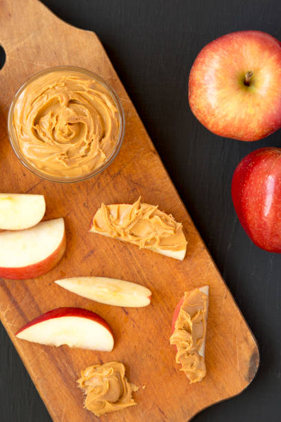istock Raw Red Apples and Peanut Butter on a rustic wooden board on a black background, top view. Flat lay, overhead, from above. 1324347648