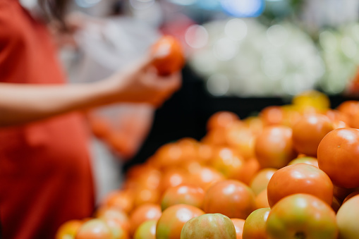 Image of an Asian woman buying fresh tomatoes in supermarket