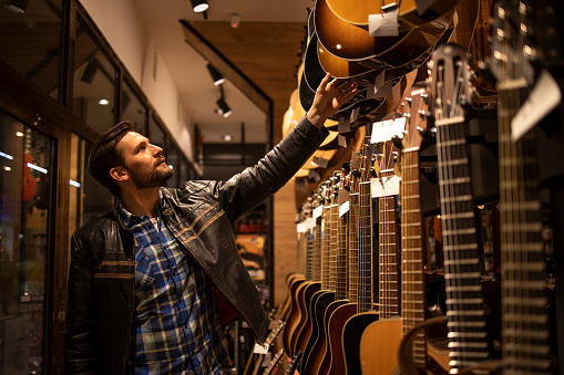 Talented musician in leather jacket searching for perfect guitar in music shop.