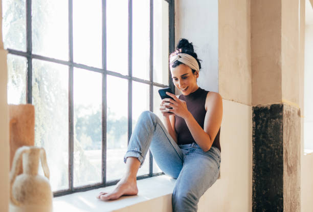 istock Cheerful Woman Siting by the Window and Using Mobile Phone 1324350563