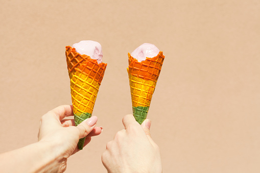 rainbow ice cream cone - two hands holdling ice cream cones in rainbow colors at hot summer day near pink background