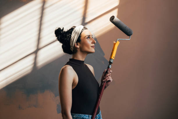 lächelnde frau posiert mit paint roller - repairing apartment home improvement painting stock-fotos und bilder