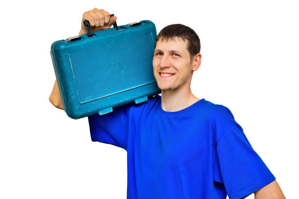 A young worker in a blue T-shirt holds a suitcase with tools on his shoulder and smiles. Isolated portrait on a white background. Urgent repairs on call.